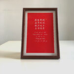 Frontal view of red paper romantic Chinese calligraphy print in dark wood frame on clean desk