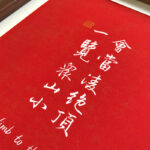 Close-up of white Chinese calligraphy characters and gold seal stamp on textured red art paper
