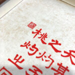 Close-up of red Xingzhuo Chinese wedding calligraphy brush strokes and red seal stamp on textured paper