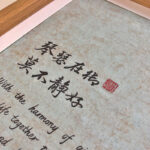 Close-up of Xingzhuo Chinese calligraphy brush strokes and red seal stamp on light green art paper