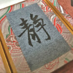 Extreme macro detail of handwritten Chinese character Quiet Jing on textured Xuan paper with Song Brocade trim.